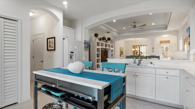 kitchen with sink, white fridge with ice dispenser, light tile patterned flooring, a tray ceiling, and white cabinets