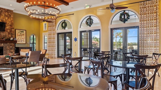 dining area featuring french doors, a fireplace, ceiling fan with notable chandelier, beamed ceiling, and a high ceiling