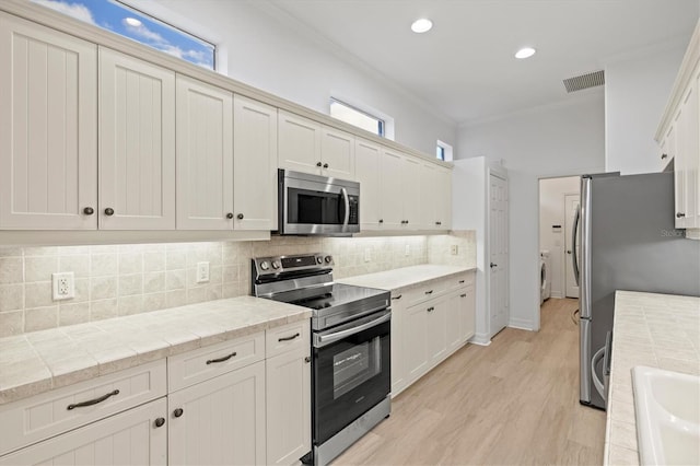 kitchen with backsplash, crown molding, separate washer and dryer, white cabinetry, and stainless steel appliances