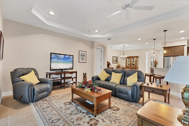 living room featuring ceiling fan with notable chandelier, a raised ceiling, and light tile patterned flooring