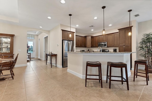 kitchen with pendant lighting, light stone countertops, an island with sink, and appliances with stainless steel finishes