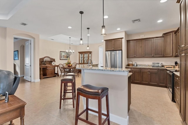 kitchen featuring pendant lighting, a kitchen bar, an island with sink, light stone counters, and stainless steel appliances