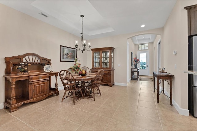 dining area with a tray ceiling, light tile patterned floors, and an inviting chandelier