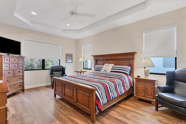 bedroom featuring light hardwood / wood-style floors, ceiling fan, and a tray ceiling