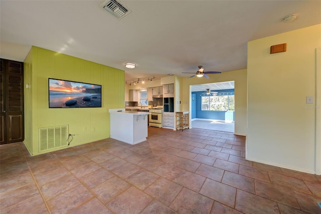 kitchen featuring kitchen peninsula, ceiling fan, light tile patterned floors, gas range gas stove, and white cabinetry