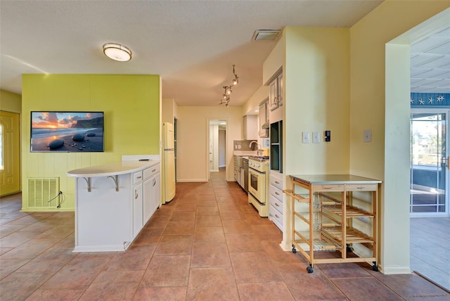 kitchen featuring white appliances, sink, light tile patterned floors, white cabinetry, and a breakfast bar area