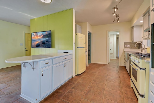 kitchen featuring a kitchen breakfast bar, gas stove, sink, white refrigerator, and white cabinets