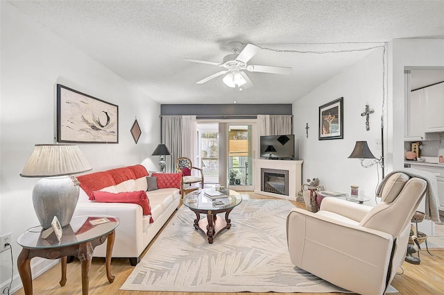 living room with ceiling fan, light wood-type flooring, and a textured ceiling