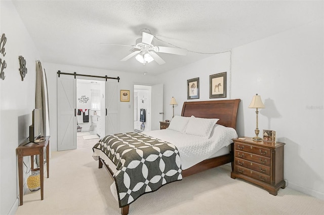 carpeted bedroom with ensuite bath, ceiling fan, and a barn door