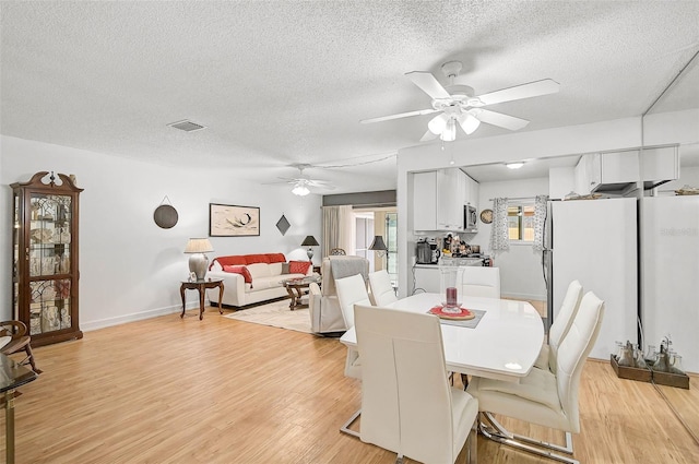 dining area featuring ceiling fan, light wood-type flooring, and a textured ceiling