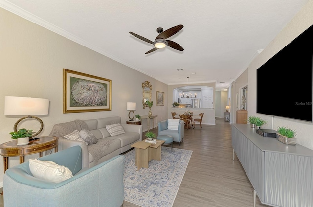 living room with light hardwood / wood-style floors, ceiling fan with notable chandelier, and ornamental molding