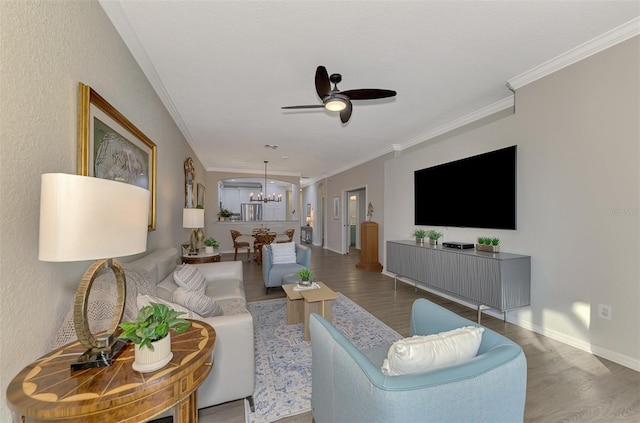 living room with wood-type flooring, ceiling fan with notable chandelier, and ornamental molding