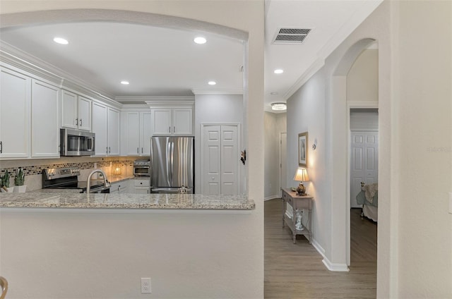 kitchen featuring appliances with stainless steel finishes, tasteful backsplash, light stone counters, crown molding, and white cabinets