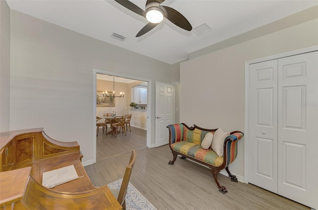 living area featuring ceiling fan with notable chandelier and light wood-type flooring