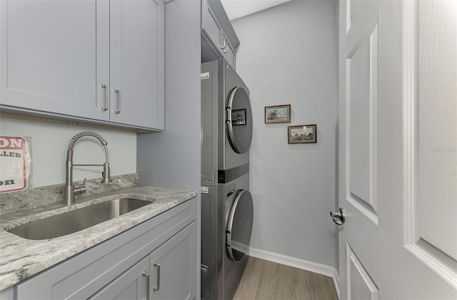 washroom featuring sink, cabinets, stacked washer / drying machine, and light wood-type flooring