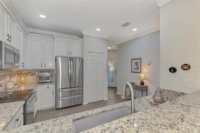 kitchen featuring light stone countertops, appliances with stainless steel finishes, white cabinetry, and ornamental molding