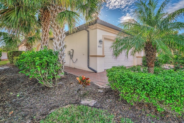 view of side of home featuring an attached garage and stucco siding