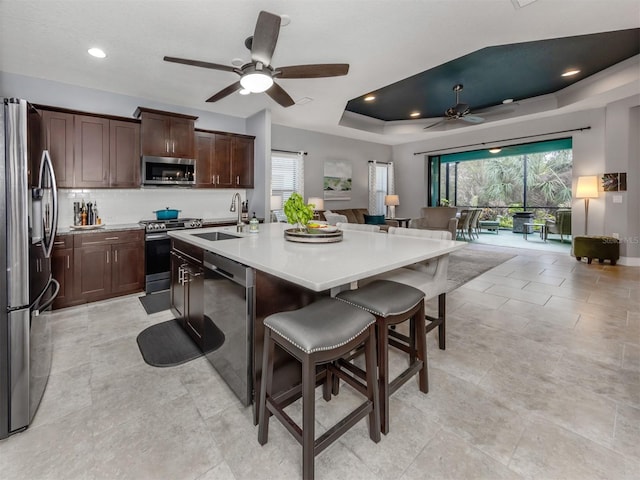 kitchen featuring a kitchen bar, stainless steel appliances, a raised ceiling, a kitchen island with sink, and sink