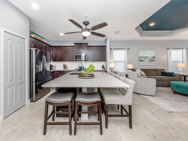 kitchen featuring appliances with stainless steel finishes, a breakfast bar, dark brown cabinets, a tray ceiling, and a kitchen island with sink