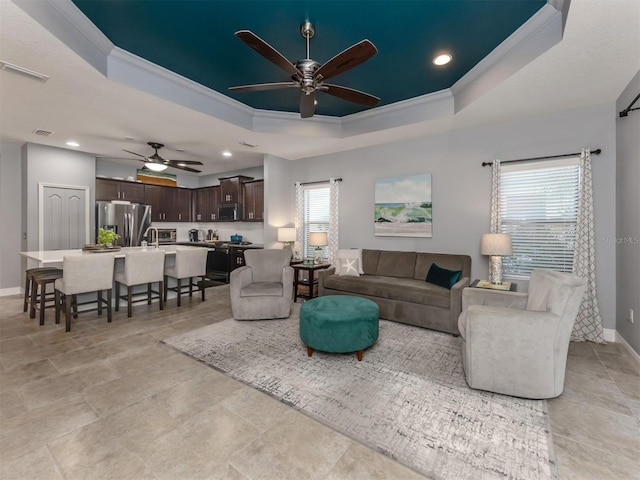 living room featuring a raised ceiling, ceiling fan, and crown molding