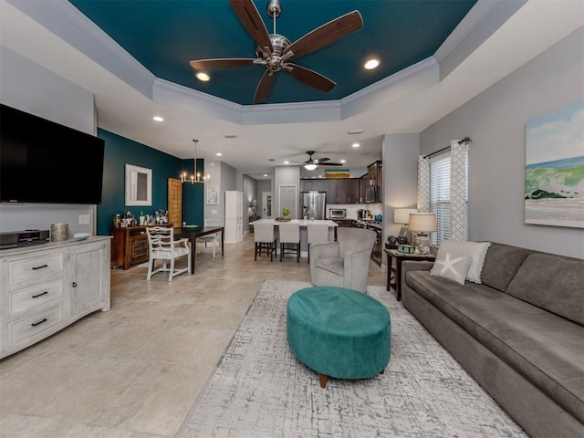 living room with ceiling fan with notable chandelier, a tray ceiling, and crown molding