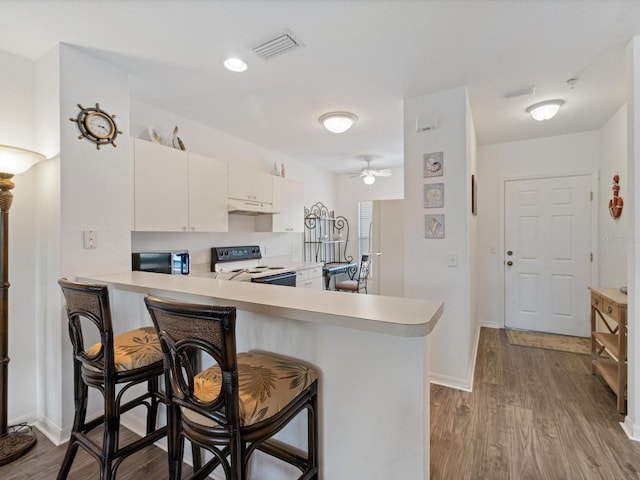 kitchen with white range with electric cooktop, a kitchen breakfast bar, kitchen peninsula, ceiling fan, and white cabinetry