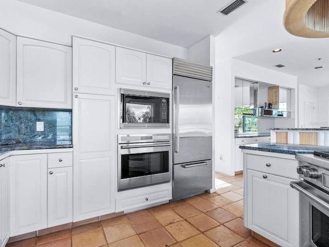 kitchen featuring white cabinets, built in appliances, tasteful backsplash, and light tile patterned flooring