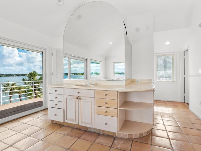 kitchen with kitchen peninsula, light tile patterned floors, a water view, and vaulted ceiling