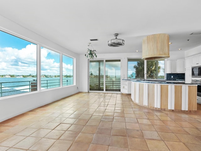 kitchen with a notable chandelier, decorative backsplash, a water view, and light tile patterned floors