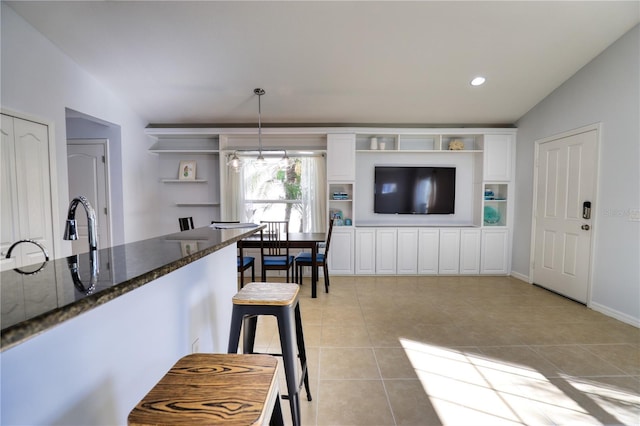 kitchen with white cabinetry, dark stone counters, pendant lighting, vaulted ceiling, and light tile patterned floors