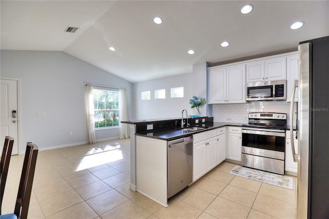 kitchen with kitchen peninsula, appliances with stainless steel finishes, vaulted ceiling, sink, and white cabinets