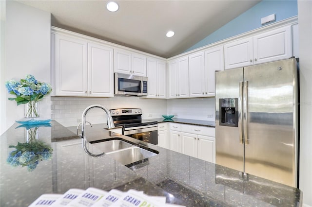 kitchen with appliances with stainless steel finishes, dark stone counters, white cabinetry, and lofted ceiling