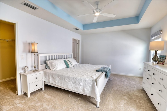 carpeted bedroom featuring a raised ceiling, a spacious closet, a closet, and ceiling fan