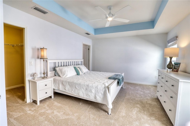 carpeted bedroom featuring a raised ceiling, a walk in closet, ceiling fan, and a closet