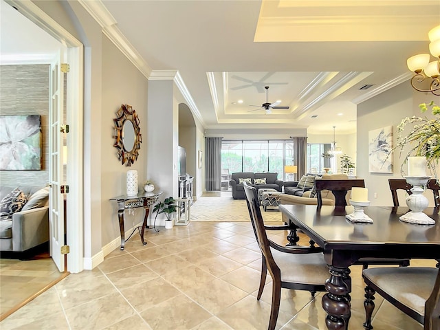 dining space with ceiling fan with notable chandelier, light tile patterned floors, crown molding, and a tray ceiling