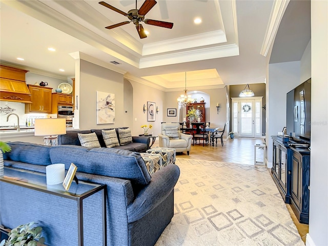 tiled living room with ceiling fan with notable chandelier, sink, crown molding, and a tray ceiling