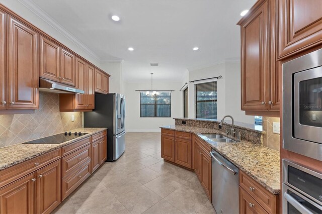 kitchen with sink, light stone counters, a notable chandelier, appliances with stainless steel finishes, and ornamental molding