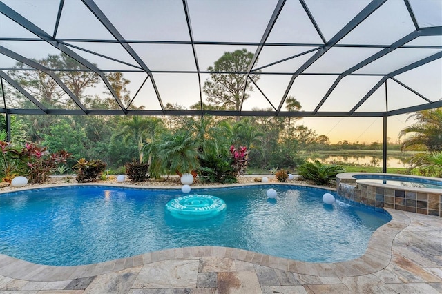 pool at dusk featuring a lanai, pool water feature, a patio area, an in ground hot tub, and a water view