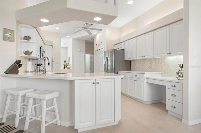 kitchen featuring white cabinetry, ceiling fan, backsplash, kitchen peninsula, and stainless steel fridge