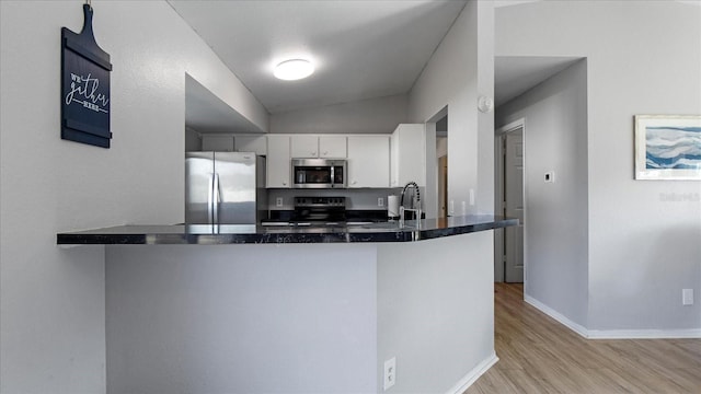 kitchen featuring kitchen peninsula, white cabinets, vaulted ceiling, and appliances with stainless steel finishes