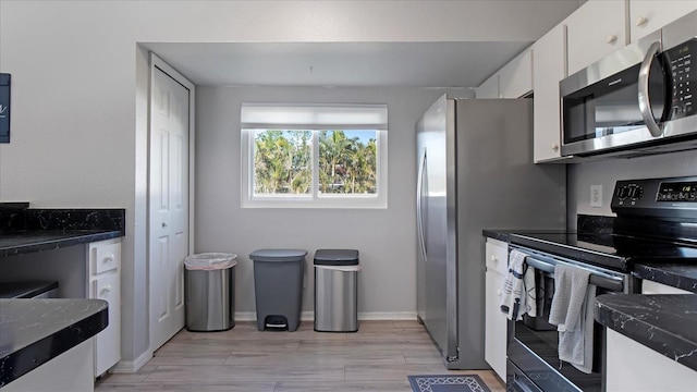 kitchen with white cabinets, light hardwood / wood-style floors, dark stone countertops, and black range with electric stovetop