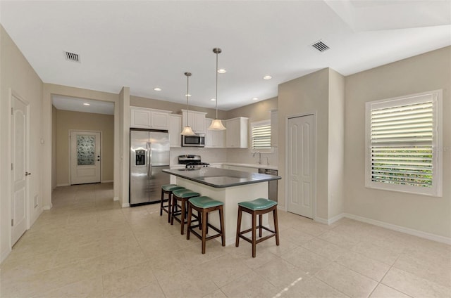 kitchen with white cabinetry, a center island, hanging light fixtures, stainless steel appliances, and a kitchen bar