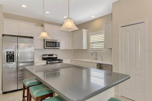 kitchen with appliances with stainless steel finishes, sink, white cabinets, a center island, and hanging light fixtures