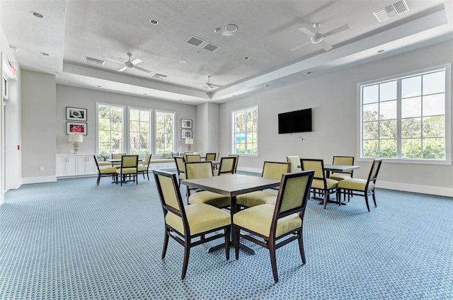 carpeted dining space with a tray ceiling and ceiling fan