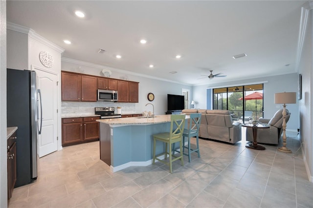 kitchen featuring a breakfast bar, sink, ceiling fan, an island with sink, and appliances with stainless steel finishes