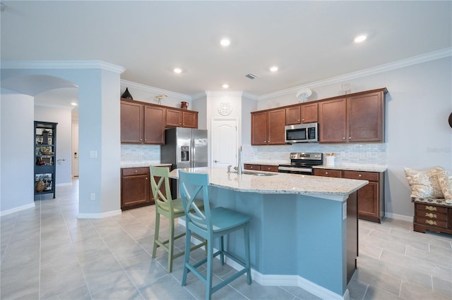 kitchen with light stone countertops, sink, an island with sink, decorative backsplash, and appliances with stainless steel finishes