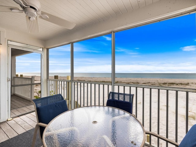 sunroom featuring ceiling fan, a water view, and a beach view