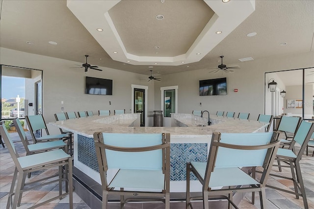 interior space featuring sink, ceiling fan, light stone countertops, a textured ceiling, and a tray ceiling