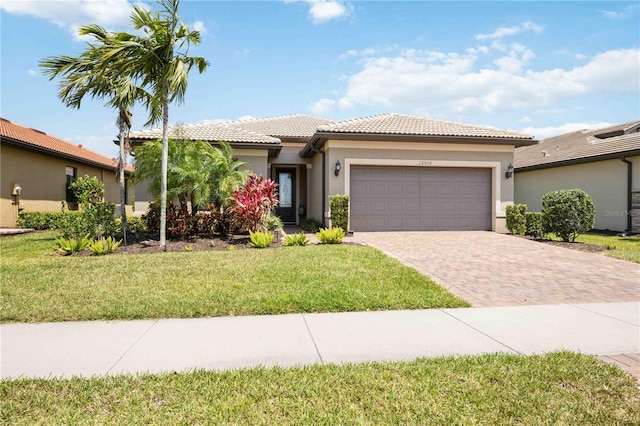 view of front facade with stucco siding, a front lawn, a tile roof, decorative driveway, and an attached garage