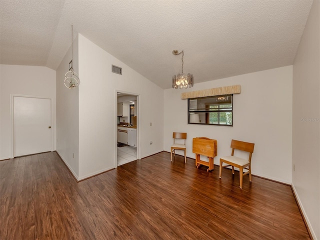 sitting room with hardwood / wood-style floors, a notable chandelier, a textured ceiling, and vaulted ceiling